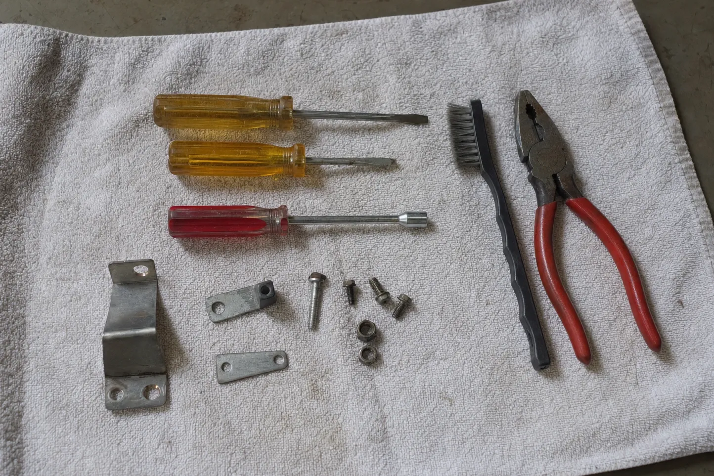 Two slotted drivers, a nut driver, wire brush and lineman’s pliers on a white towel with a bracket and link plates