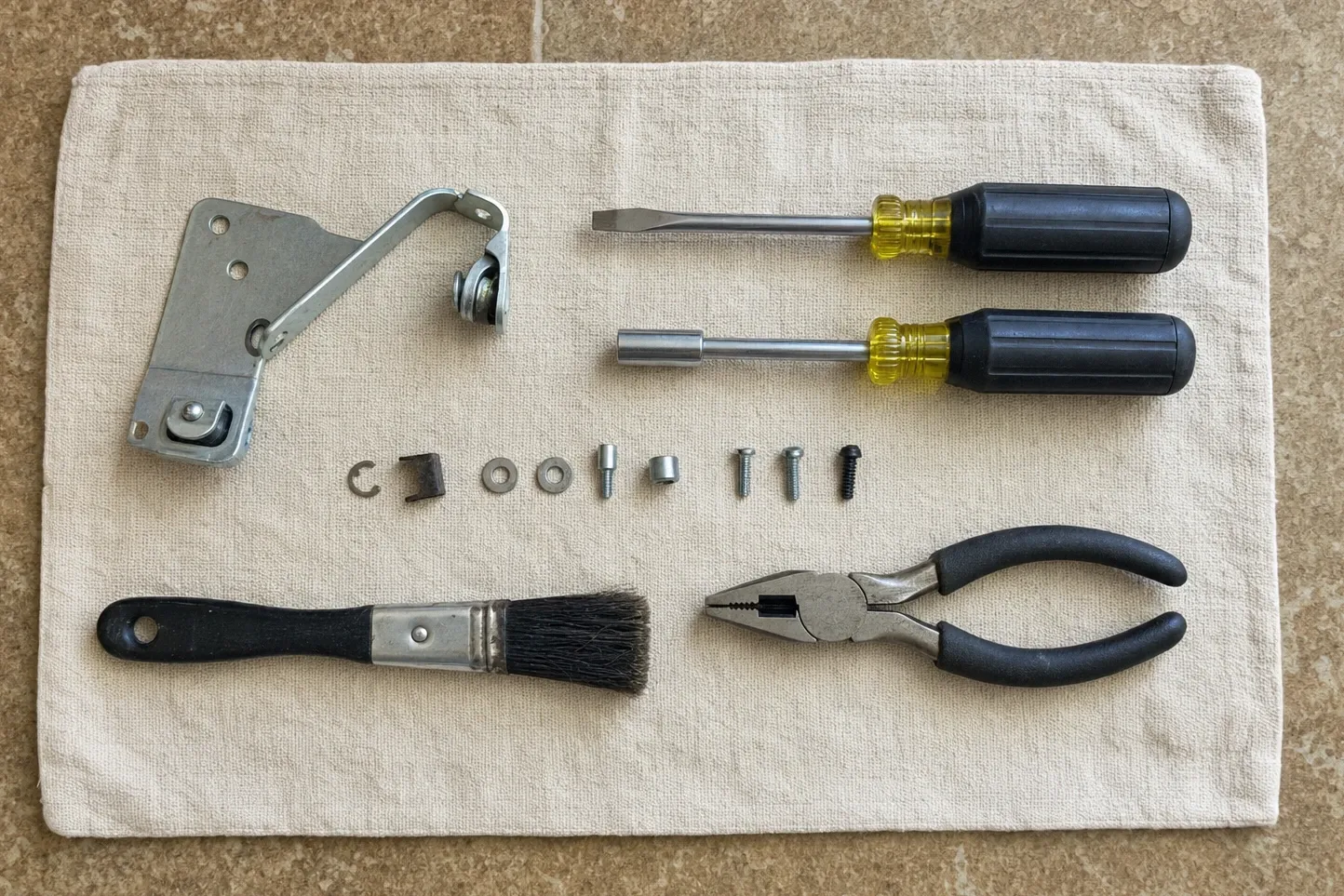Chrome door hinge with its roller laid out on cloth beside drivers, pliers, a retaining clip and its fixings